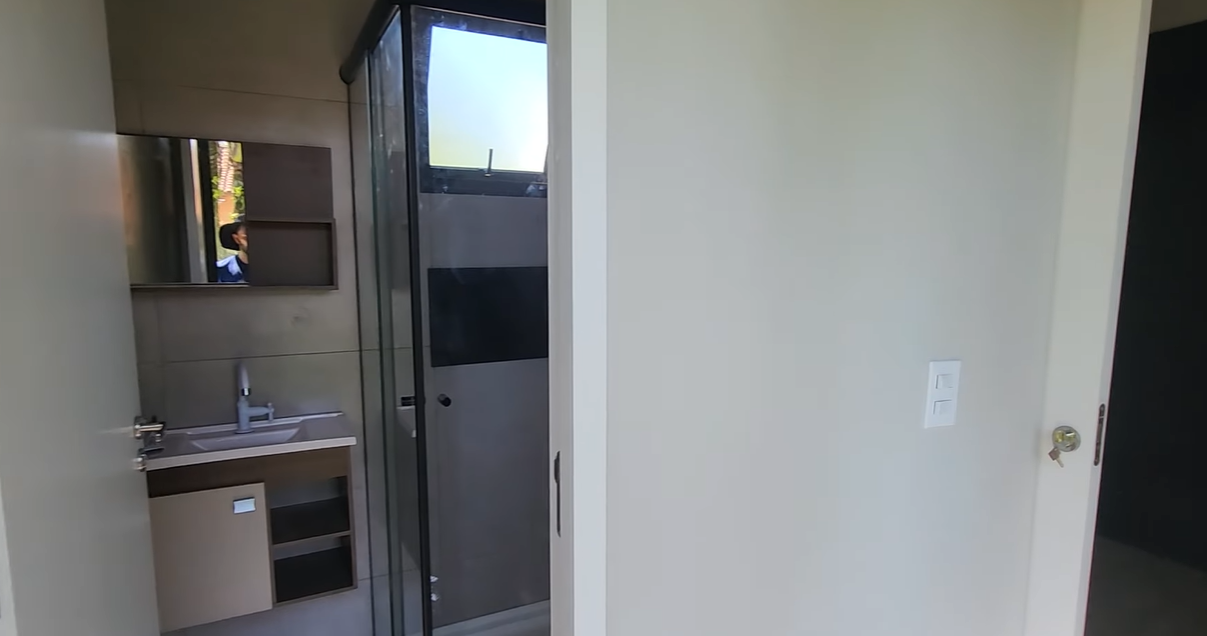 Vista do banheiro com box de vidro fumê e bancada em porcelanato